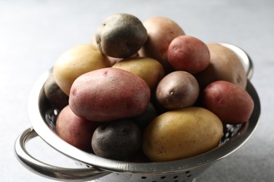 Photo of Different types of potatoes in colander on grey table, closeup