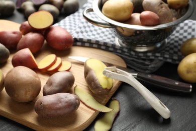 Photo of Different types of potatoes, peeler and knife on black table, closeup