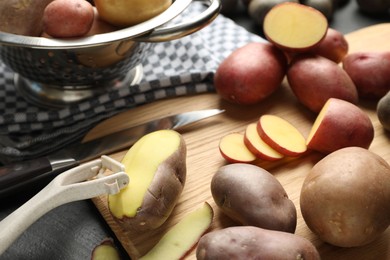 Photo of Different types of potatoes, peeler and knife on black table, closeup