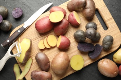 Photo of Different types of potatoes, peeler and knife on black table, flat lay