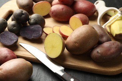 Photo of Different types of potatoes, peeler and knife on black table, closeup