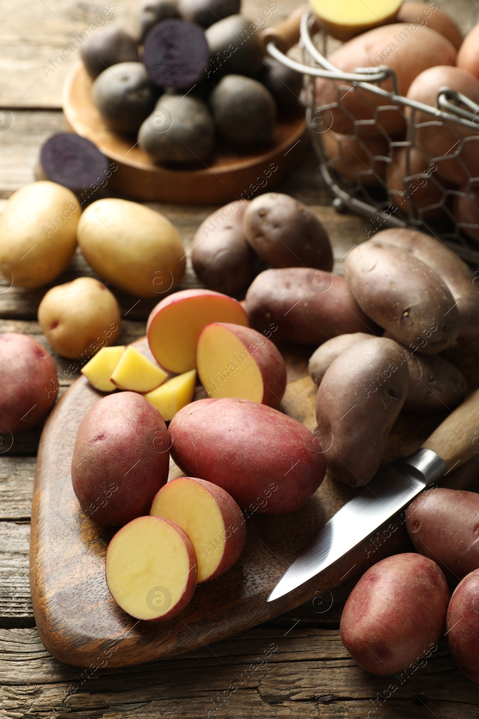 Photo of Different types of potatoes and knife on wooden table, closeup