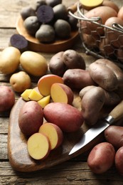 Photo of Different types of potatoes and knife on wooden table, closeup