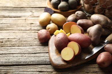 Photo of Different types of potatoes and knife on wooden table, closeup. Space for text