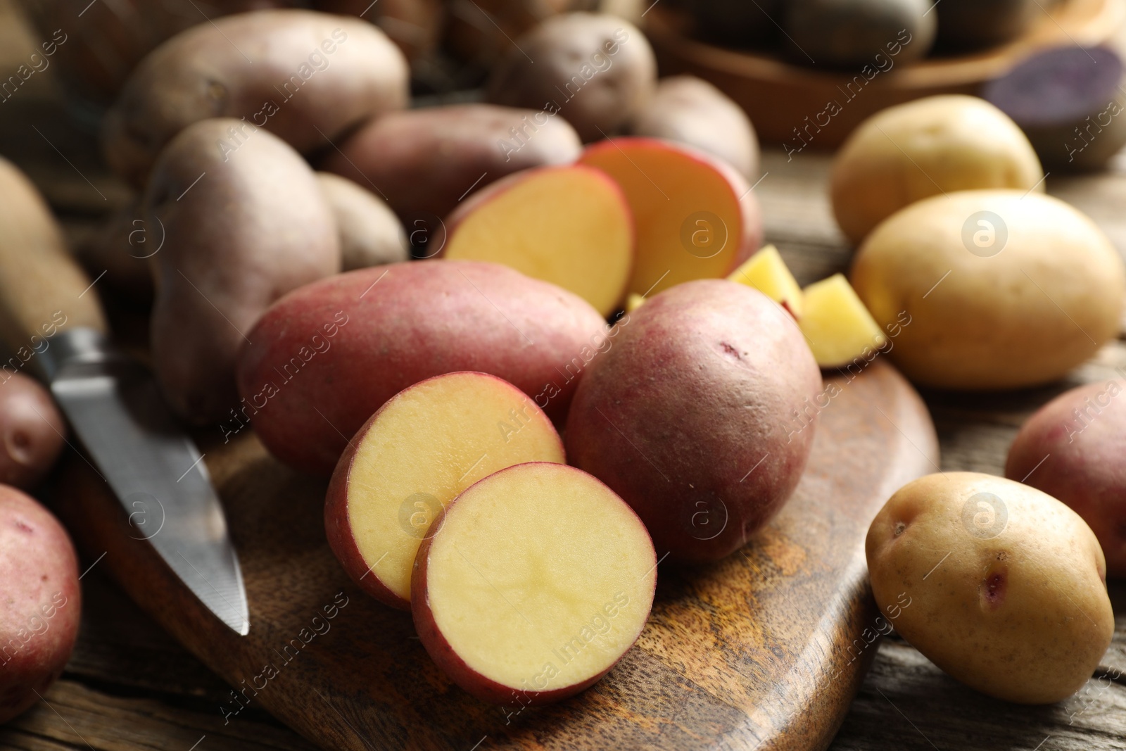 Photo of Different types of potatoes and knife on wooden table, closeup