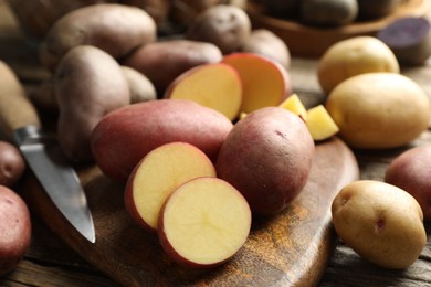 Photo of Different types of potatoes and knife on wooden table, closeup