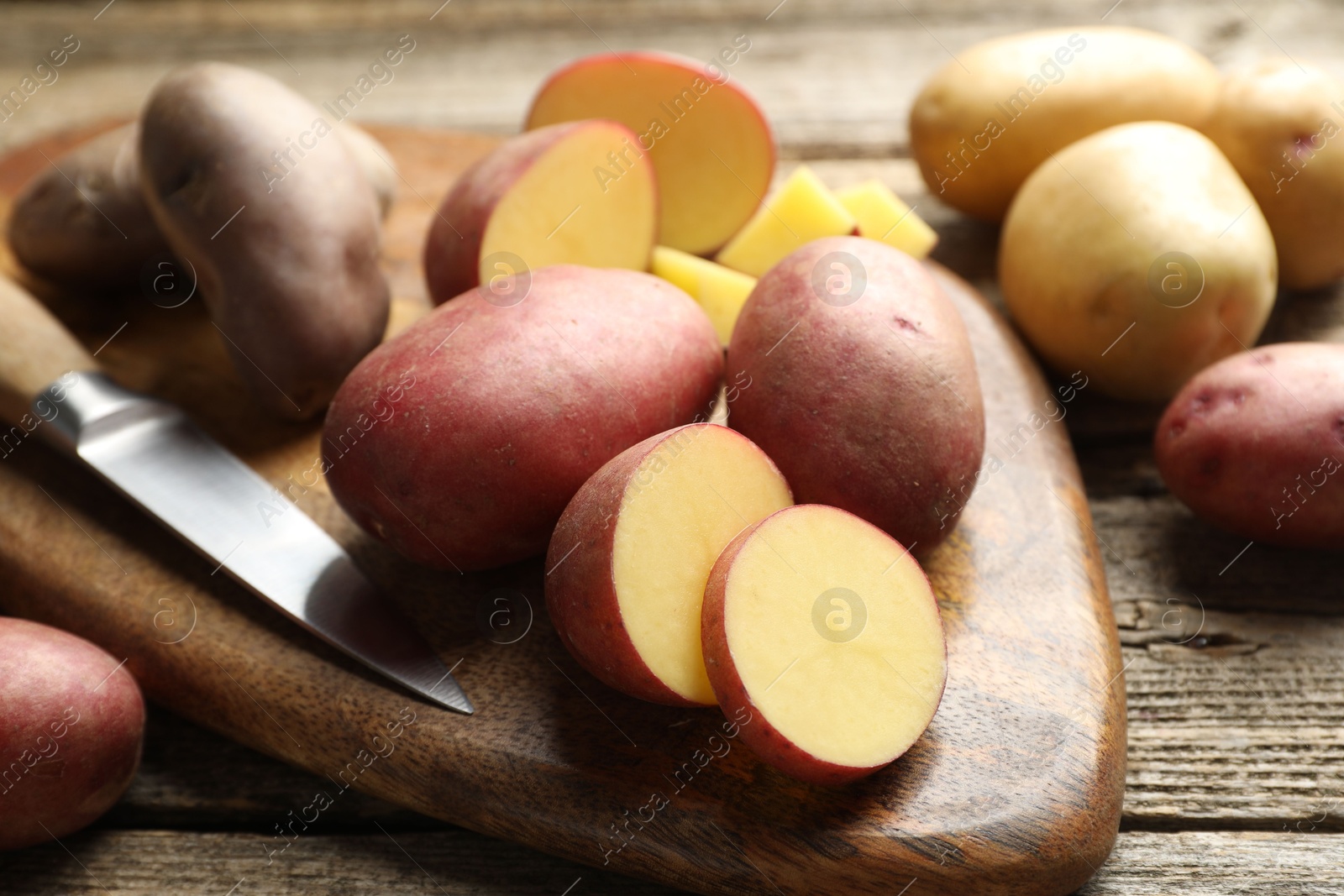 Photo of Different types of potatoes and knife on wooden table, closeup