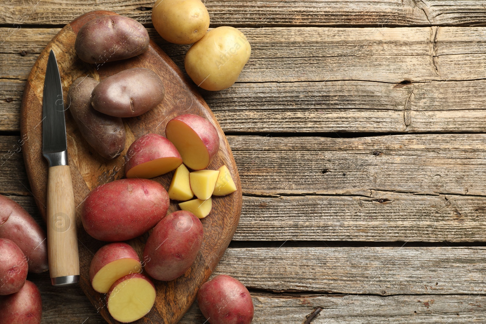 Photo of Different types of potatoes and knife on wooden table, flat lay. Space for text