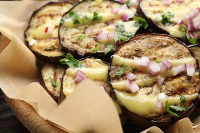 Photo of Grilled slices of eggplant with sauce, parsley and onion served on wooden table, closeup