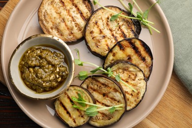Photo of Grilled slices of eggplant with sauce and microgreens on wooden table, top view
