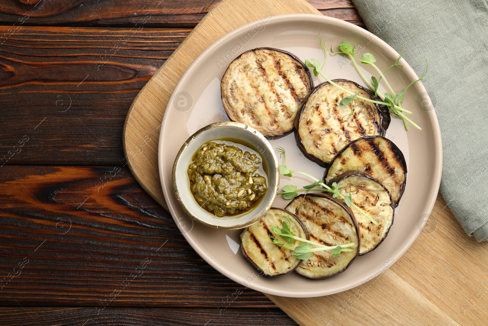 Photo of Grilled slices of eggplant with sauce and microgreens on wooden table, top view