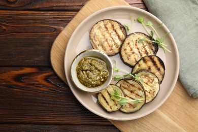 Photo of Grilled slices of eggplant with sauce and microgreens on wooden table, top view