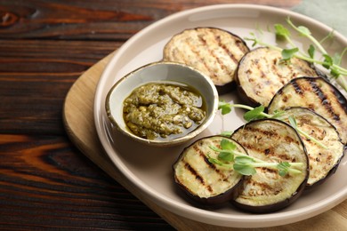 Photo of Grilled slices of eggplant with sauce and microgreens on wooden table, closeup