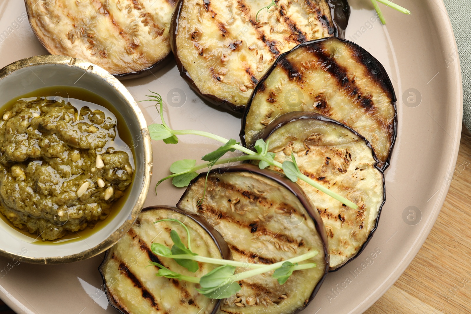 Photo of Grilled slices of eggplant with sauce and microgreens on wooden table, top view