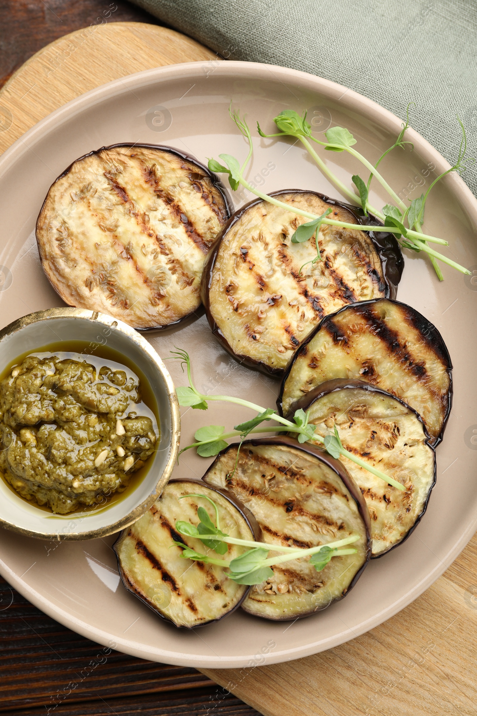 Photo of Grilled slices of eggplant with sauce and microgreens on wooden table, top view