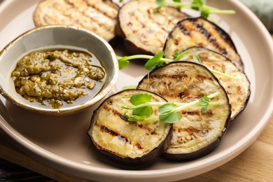 Photo of Grilled slices of eggplant with sauce and microgreens on wooden table, closeup