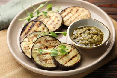 Photo of Grilled slices of eggplant with sauce and microgreens on wooden table, closeup