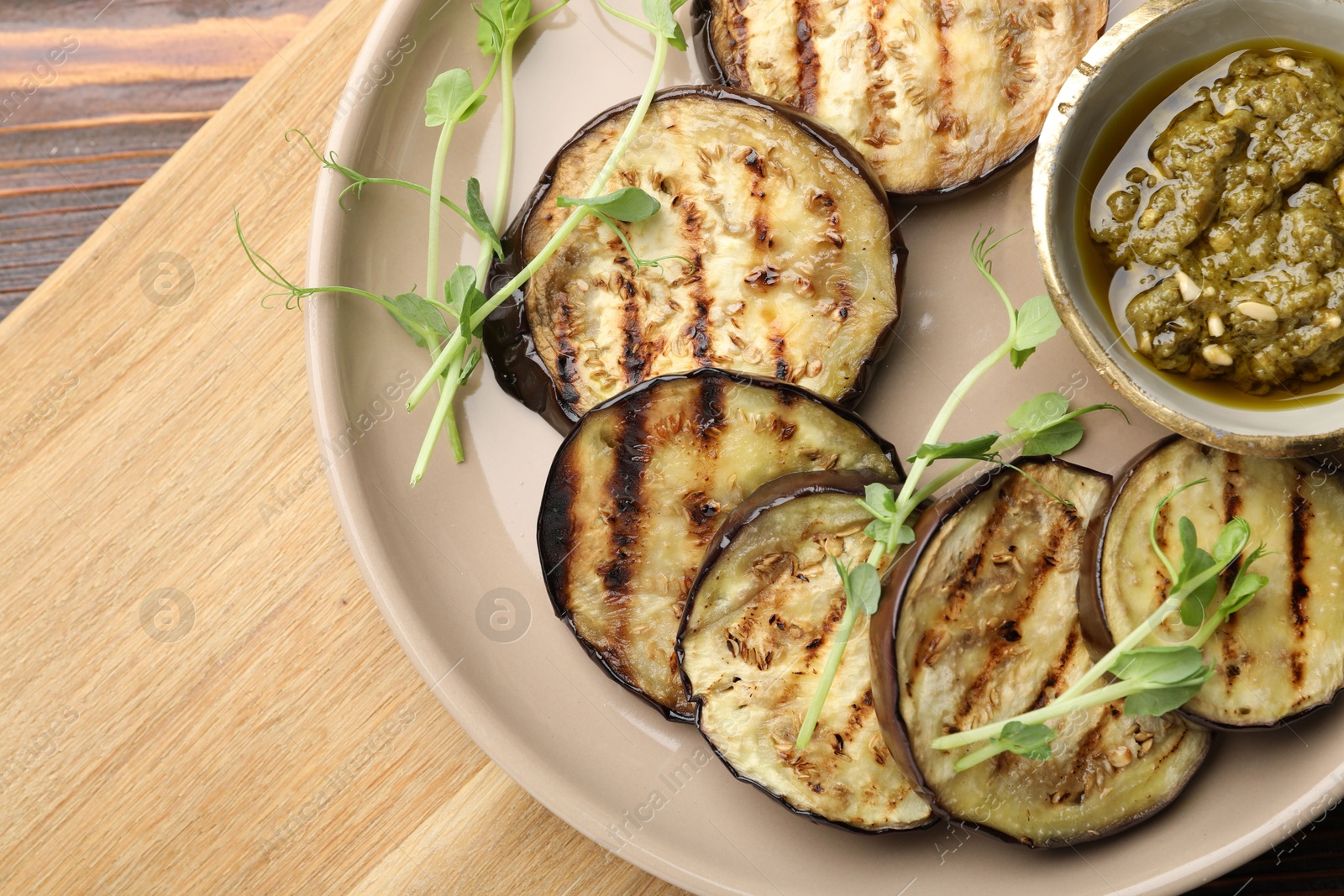 Photo of Grilled slices of eggplant with sauce and microgreens on wooden table, top view