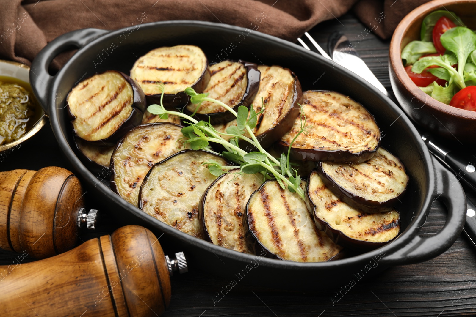 Photo of Grilled slices of eggplant with microgreens served on wooden table, closeup