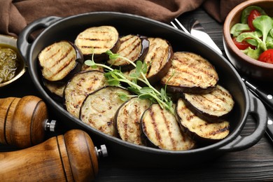Photo of Grilled slices of eggplant with microgreens served on wooden table, closeup