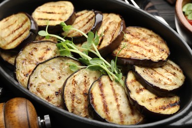Photo of Grilled slices of eggplant with microgreens served on wooden table, closeup