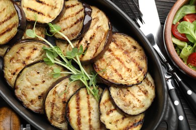 Photo of Grilled slices of eggplant with microgreens served on wooden table, closeup