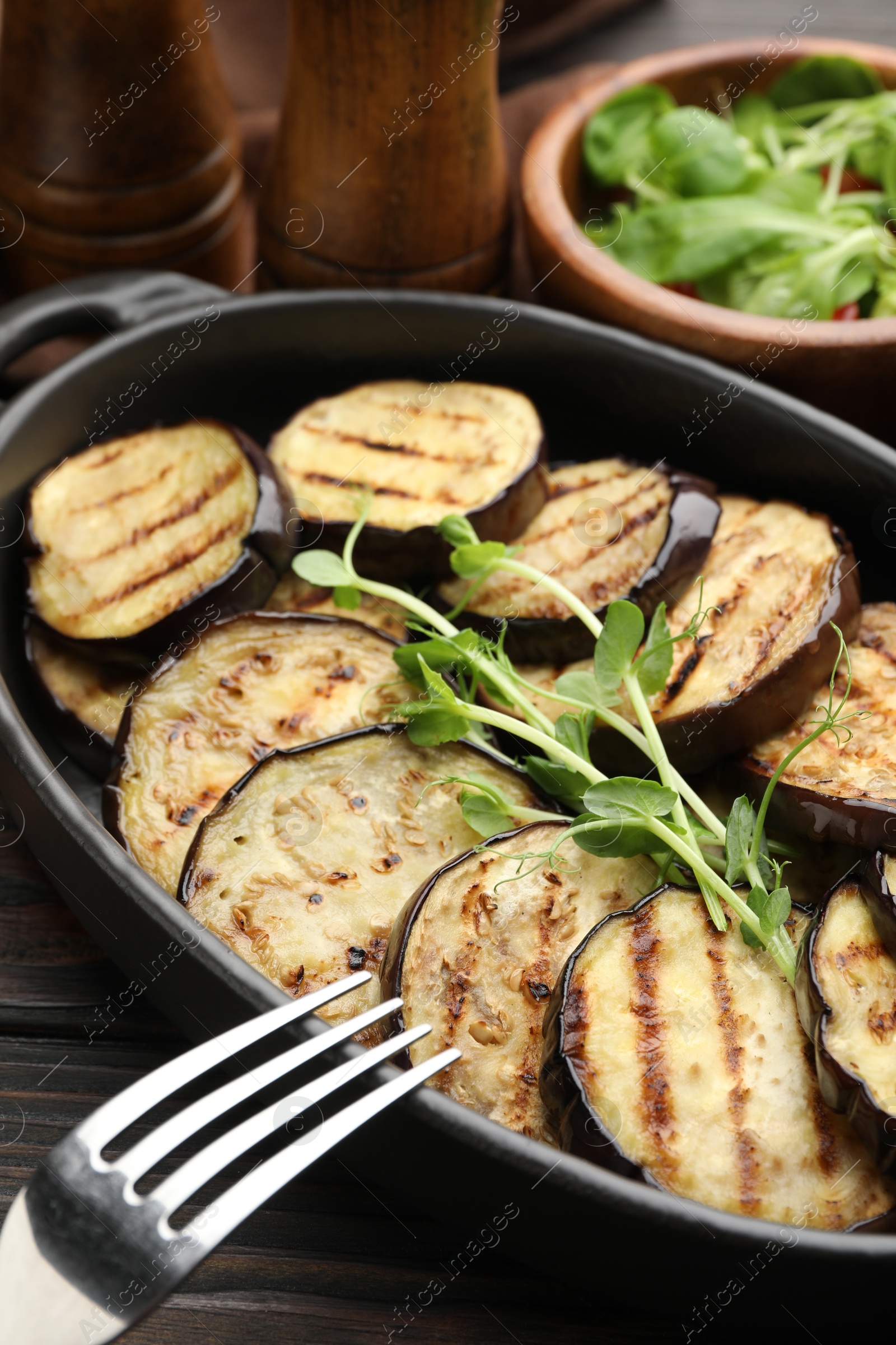 Photo of Grilled slices of eggplant with microgreens served on wooden table, closeup