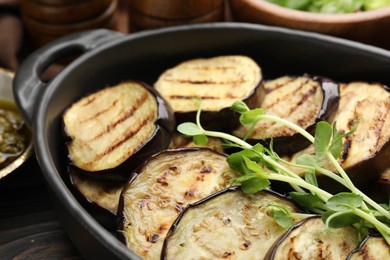 Photo of Grilled slices of eggplant with microgreens served on wooden table, closeup
