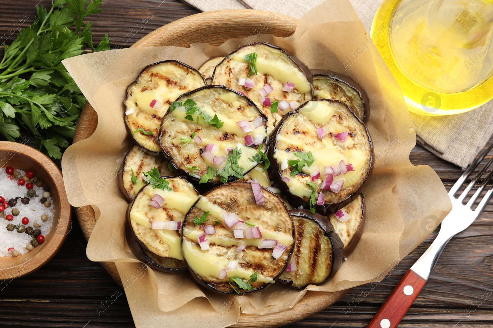 Photo of Grilled slices of eggplant with sauce, parsley and onion served on wooden table, flat lay