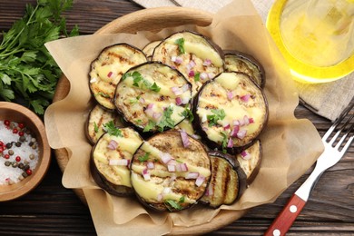 Photo of Grilled slices of eggplant with sauce, parsley and onion served on wooden table, flat lay