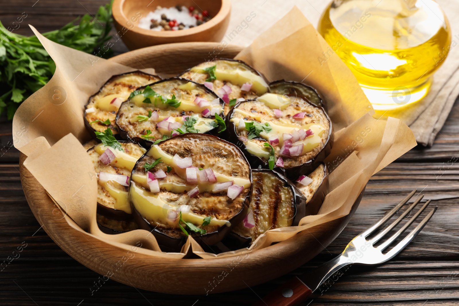 Photo of Grilled slices of eggplant with sauce, parsley and onion served on wooden table, closeup