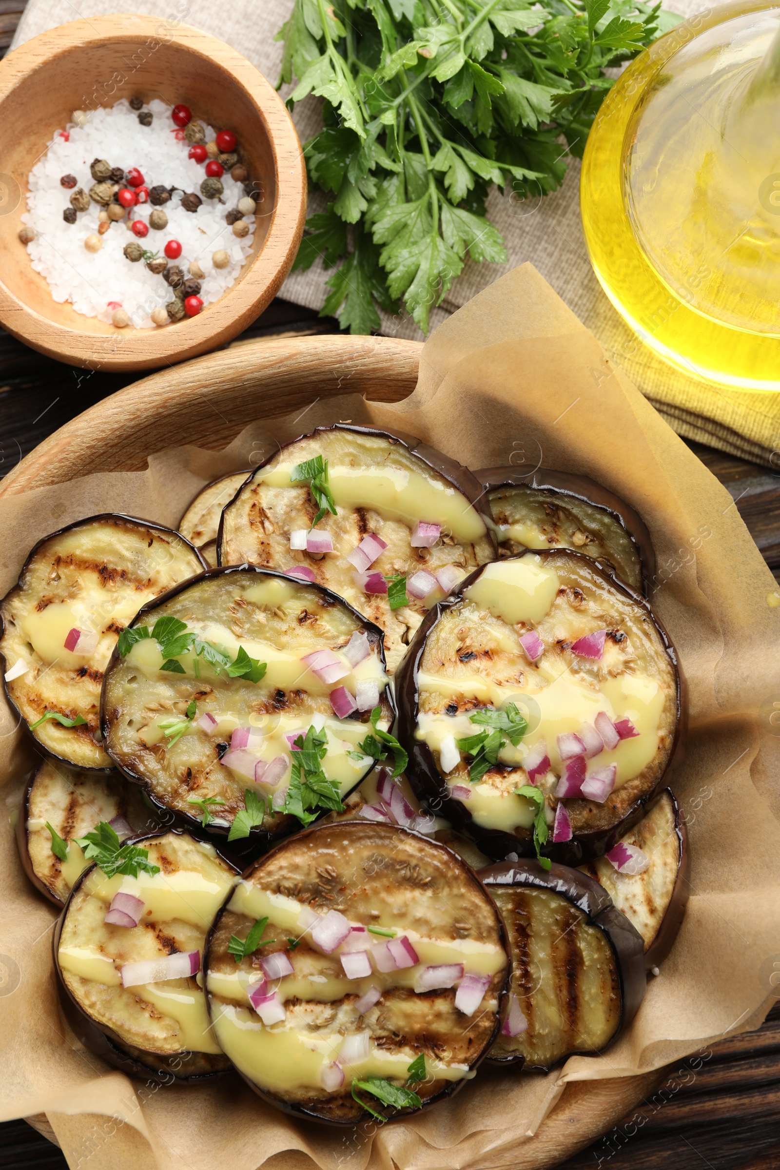 Photo of Grilled slices of eggplant with sauce, parsley and onion served on wooden table, flat lay