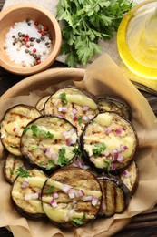 Photo of Grilled slices of eggplant with sauce, parsley and onion served on wooden table, flat lay