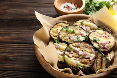 Photo of Grilled slices of eggplant with sauce, parsley and onion served on wooden table, closeup. Space for text