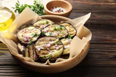 Photo of Grilled slices of eggplant with sauce, parsley and onion served on wooden table, closeup