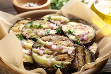 Photo of Grilled slices of eggplant with sauce, parsley and onion served on wooden table, closeup
