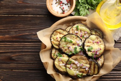 Photo of Grilled slices of eggplant with sauce, parsley and onion served on wooden table, flat lay. Space for text