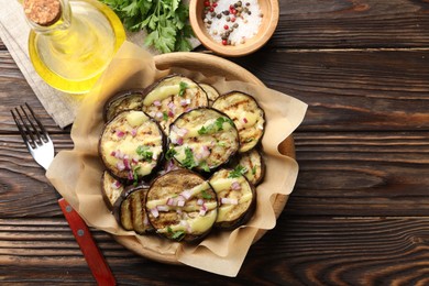 Photo of Grilled slices of eggplant with sauce, parsley and onion served on wooden table, flat lay