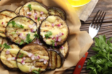 Photo of Grilled slices of eggplant with sauce, parsley and onion served on wooden table, flat lay