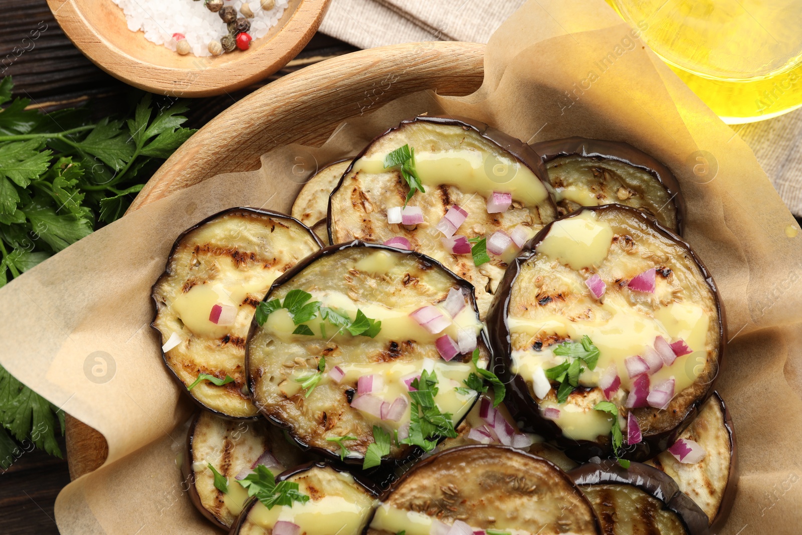 Photo of Grilled slices of eggplant with sauce, parsley and onion served on wooden table, closeup