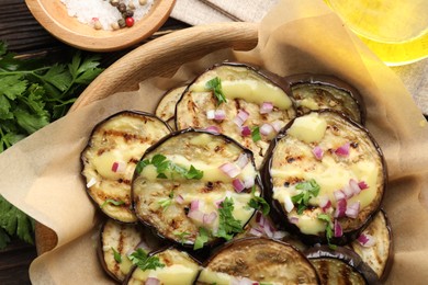 Photo of Grilled slices of eggplant with sauce, parsley and onion served on wooden table, closeup