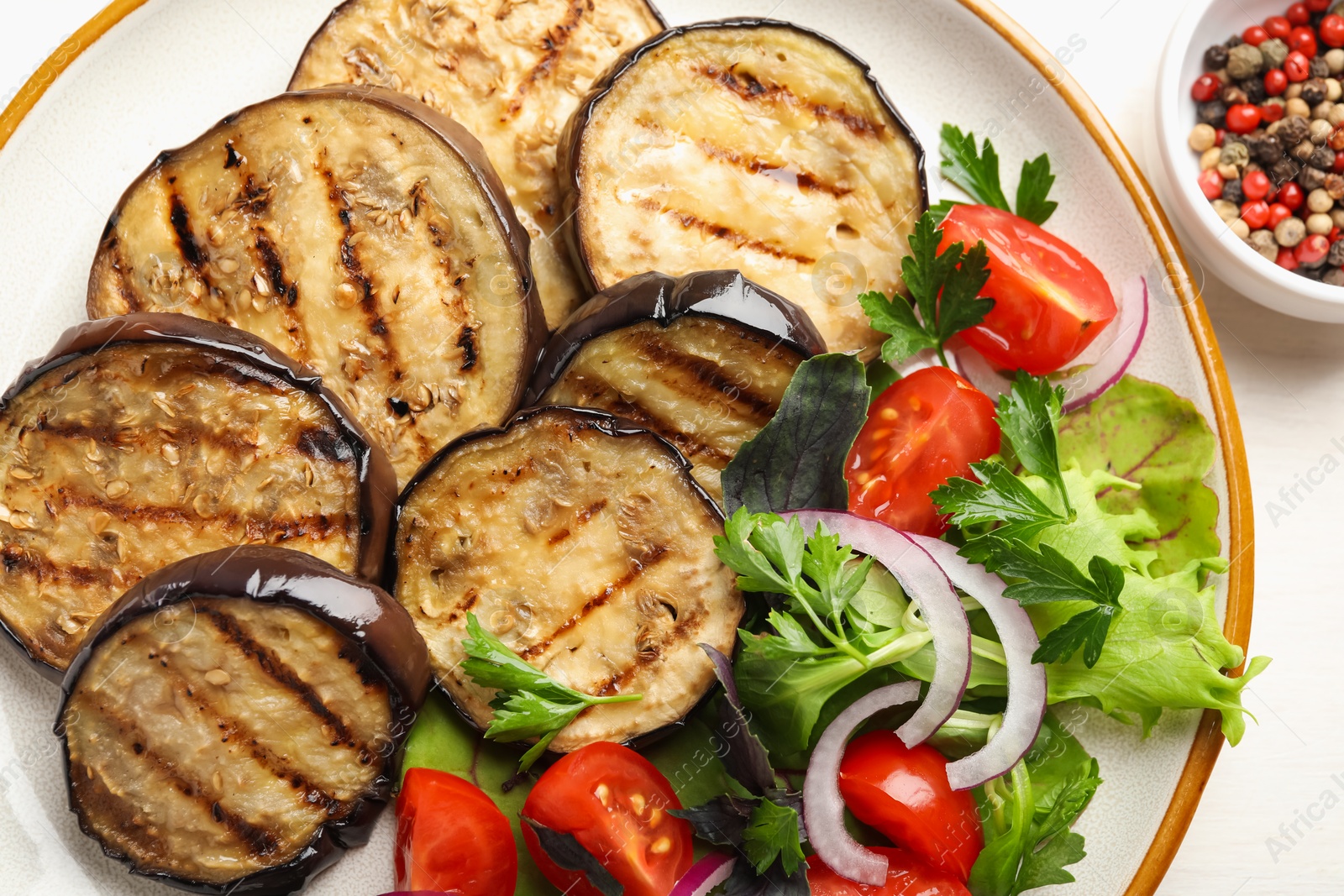 Grilled slices of eggplant with salad and peppercorns on white table, top view Photo of Grilled slices of eggplant with salad and peppercorns on white table, top view