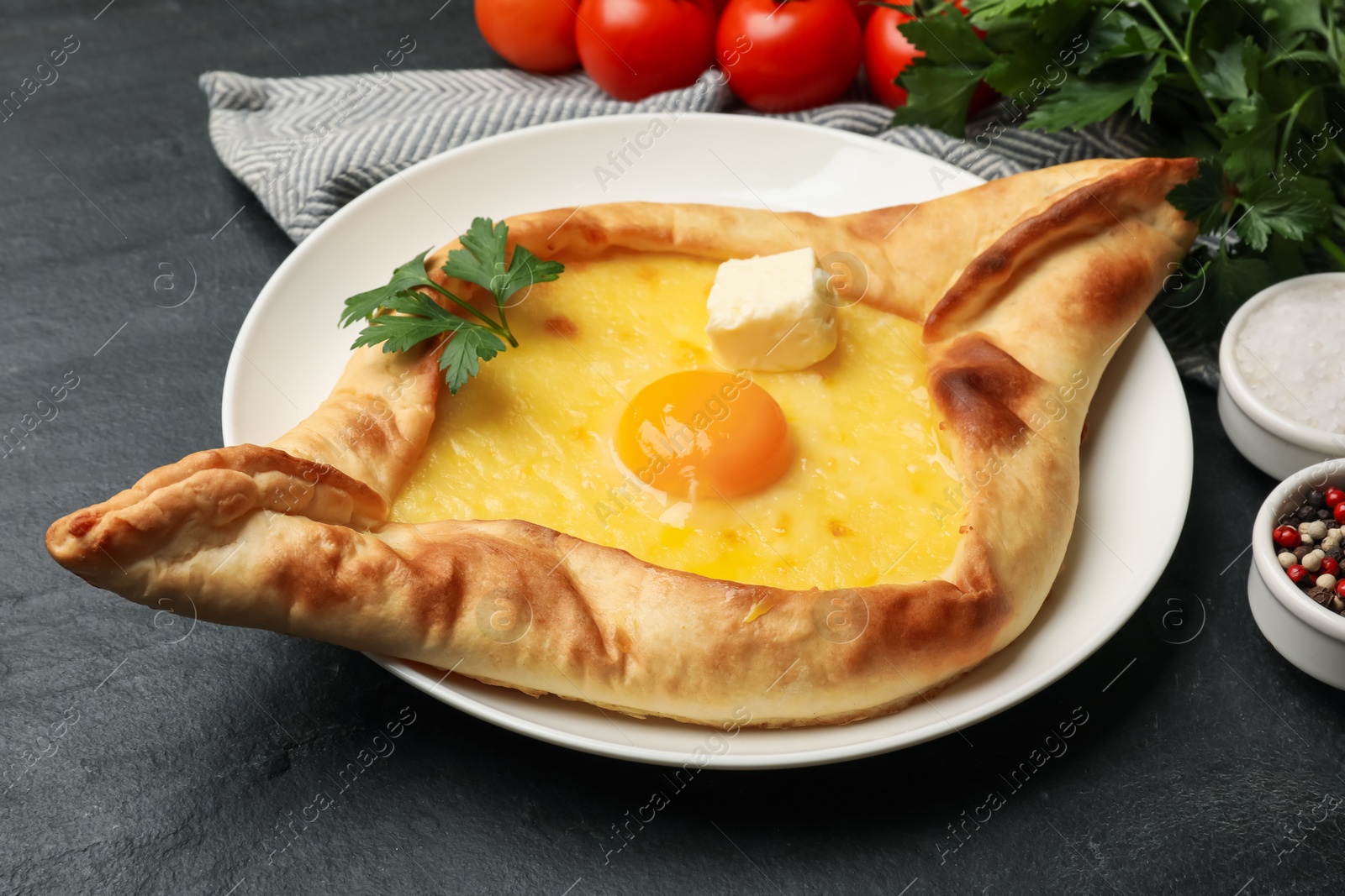 Tasty khachapuri with cheese, egg and other products on black table, closeup Photo of Tasty khachapuri with cheese, egg and other products on black table, closeup