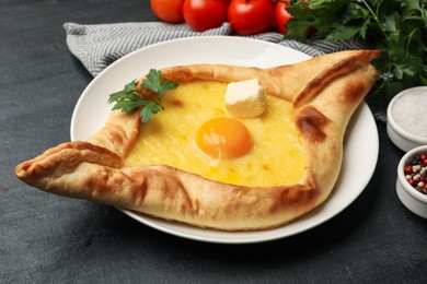 Photo of Tasty khachapuri with cheese, egg and other products on black table, closeup