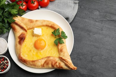 Photo of Tasty khachapuri with cheese, egg and other products on black table, flat lay. Space for text