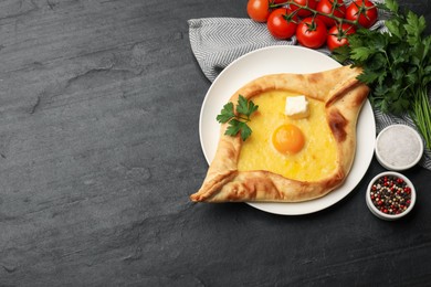 Photo of Tasty khachapuri with cheese, egg and other products on black table, flat lay. Space for text