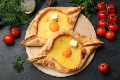 Photo of Tasty khachapuri with cheese, egg and other products on black table, flat lay