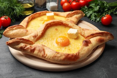 Photo of Tasty khachapuri with cheese, egg and other products on black table, closeup