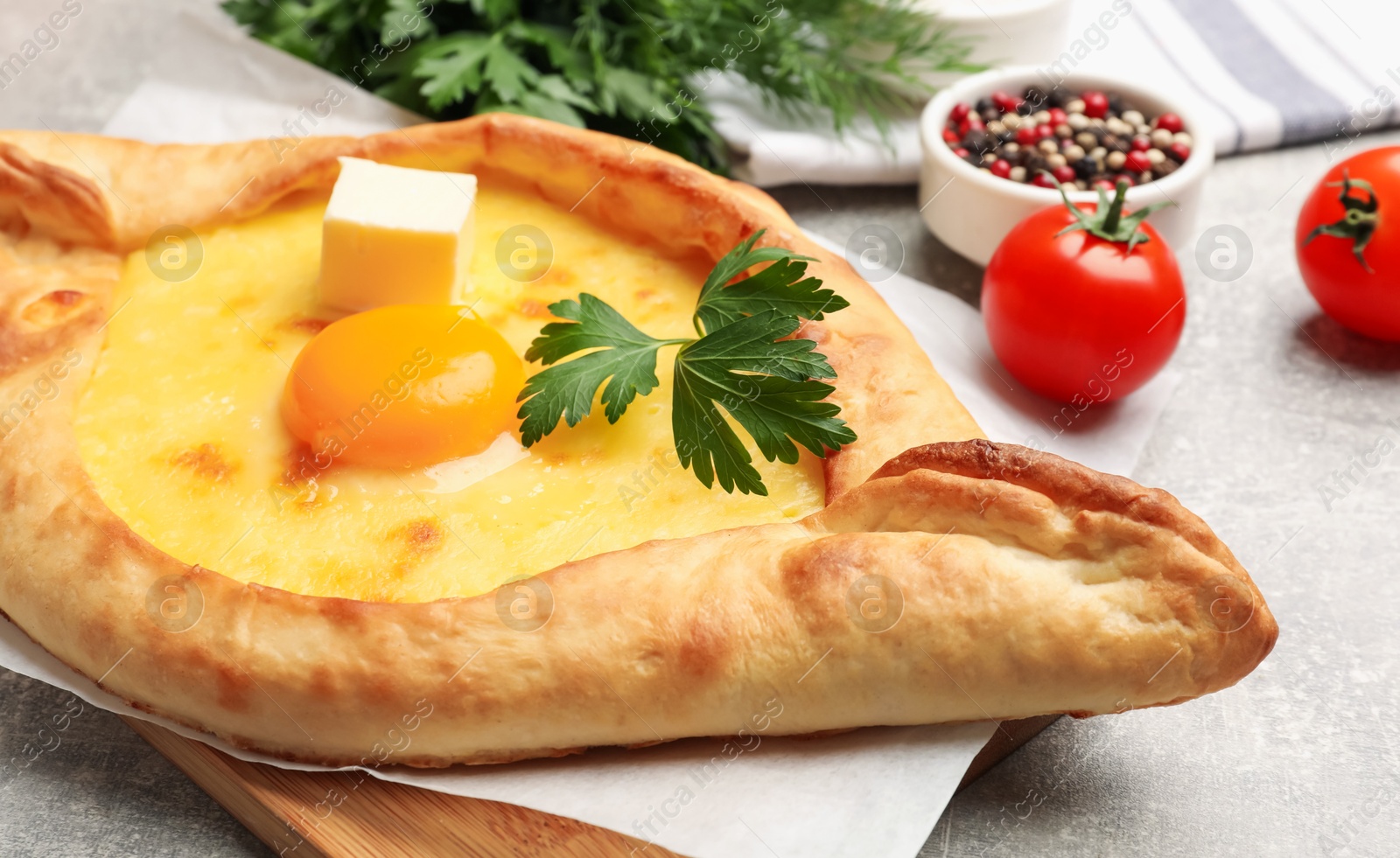 Photo of Tasty khachapuri with cheese, egg, parsley and other products on light grey background, closeup