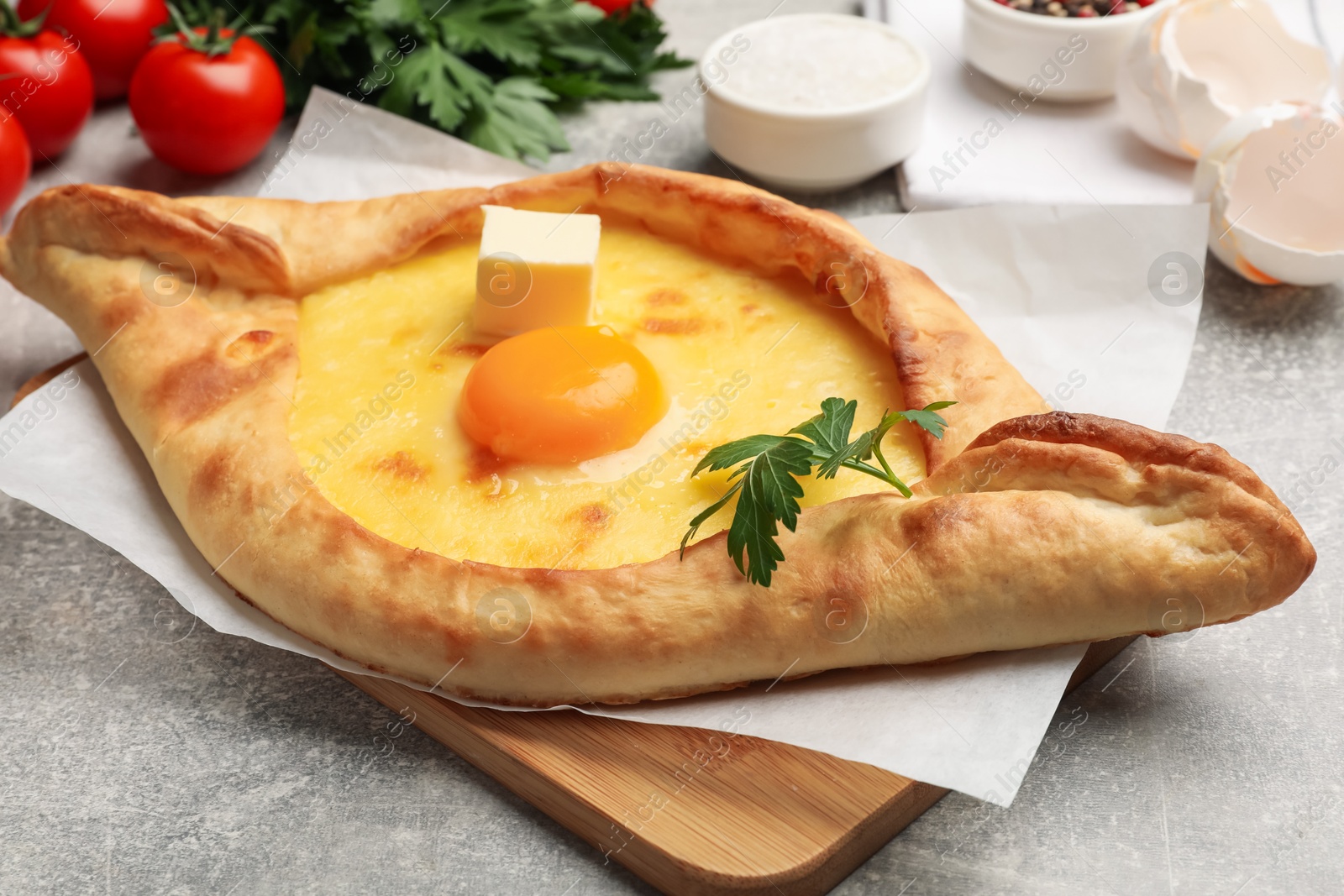 Tasty khachapuri with cheese, egg, parsley and other products on light grey background, closeup Photo of Tasty khachapuri with cheese, egg, parsley and other products on light grey background, closeup